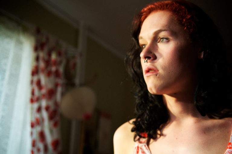Film still from "Something must Break", a person with dark red curly hair and nose ring looks thoughtful