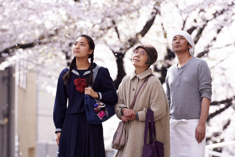 Three people admire the blossoming cherry trees