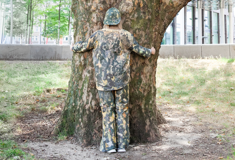 Eine Person in camouflage Kleidung umarmt einen Baum.