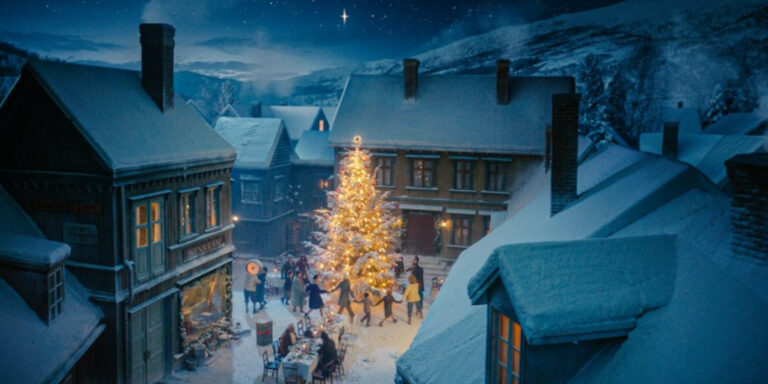 Animated image of a village at night with snow. People dancing around a glowing Christmas tree.